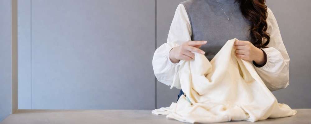 白いトップスをたたむ女性の画像