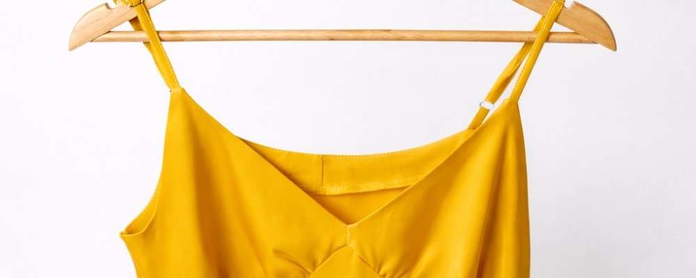 ハンガーにかけられた黄色いワンピースを持つ女性の手