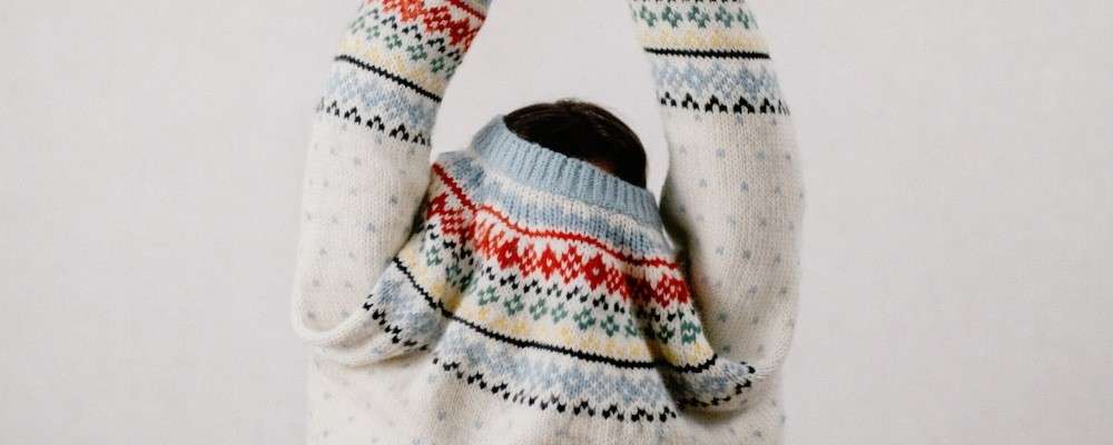 柄あふれたセーターを着た人が腕を頭上に伸ばす